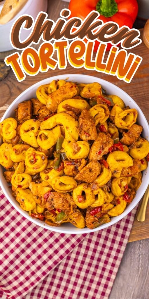 A bowl of chicken tortellini pasta on a wooden table with a red checkered napkin.