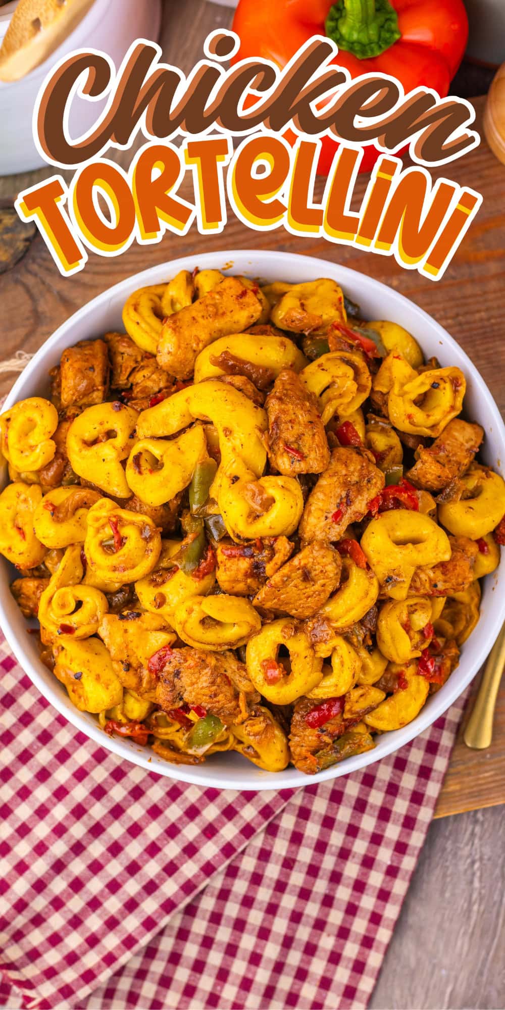A bowl of chicken tortellini pasta on a wooden table with a red checkered napkin.