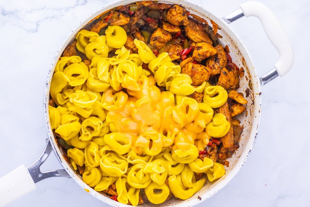A skillet with cooked chicken, vegetables, and cheese tortellini mixed together.