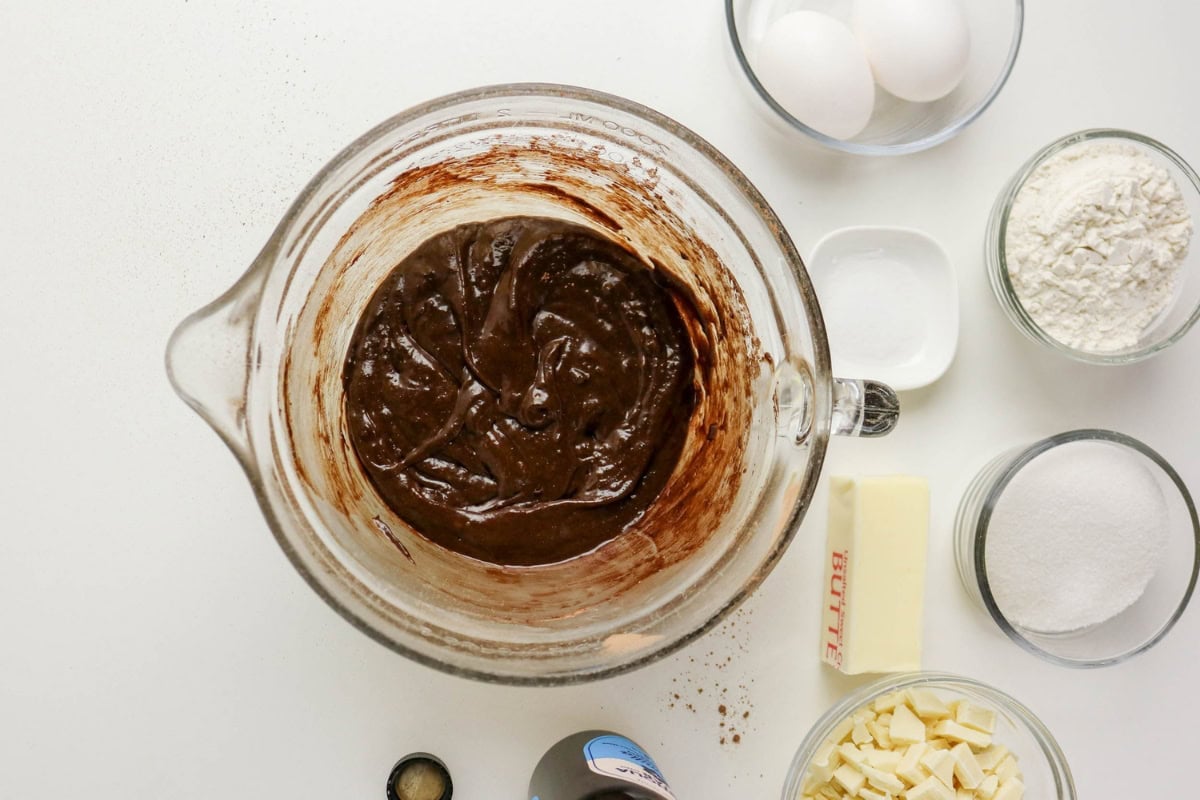 A glass bowl of chocolate batter with baking ingredients arranged around it.