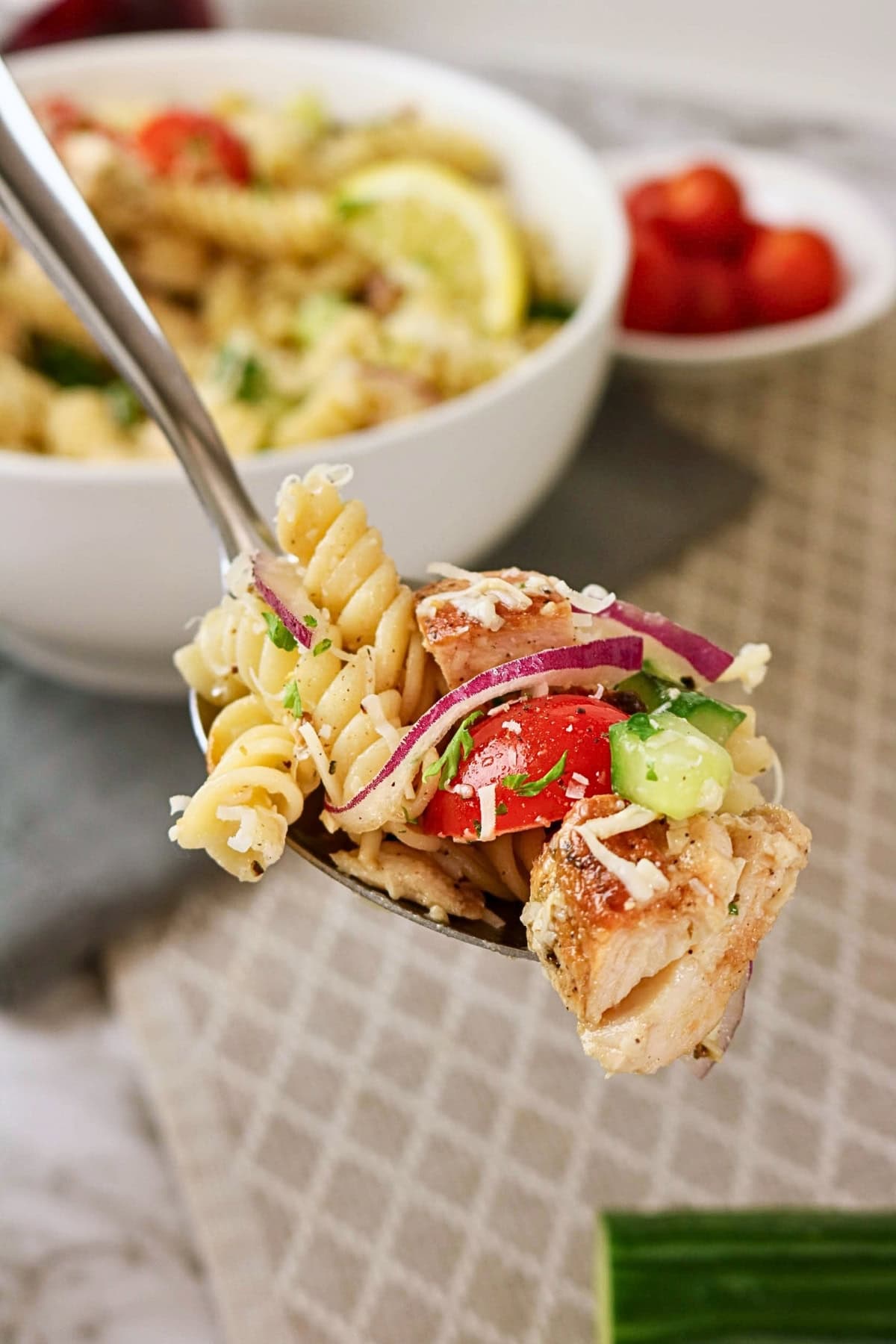 A spoonful of pasta salad with grilled chicken, tomato, onion, and cucumber.