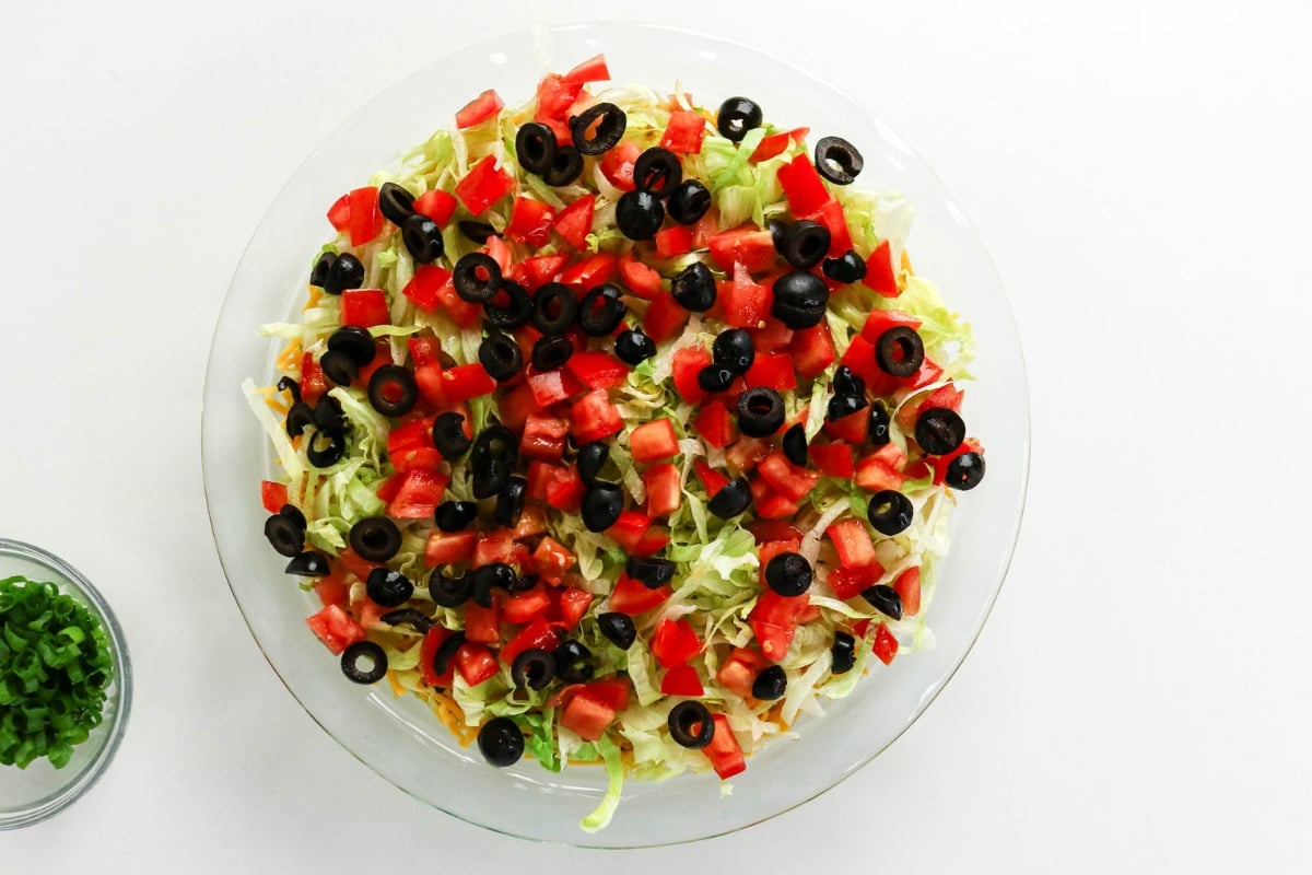 A glass bowl of salad with lettuce, tomatoes, black olives, and cheese.