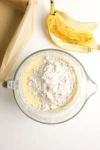 A mixing bowl with flour on batter, a banana peel, and a lined baking pan.