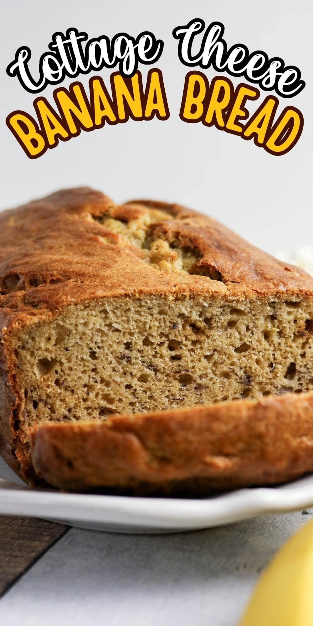 A loaf of cottage cheese banana bread with one slice cut, on a white plate.