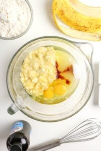Ingredients for banana bread, including eggs and mashed banana, in a glass mixing bowl.