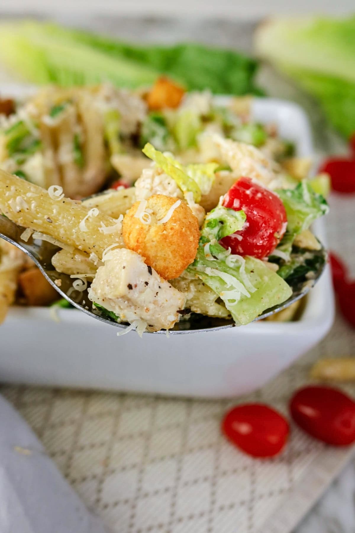 A spoonful of pasta salad with chicken, lettuce, tomatoes, and croutons.