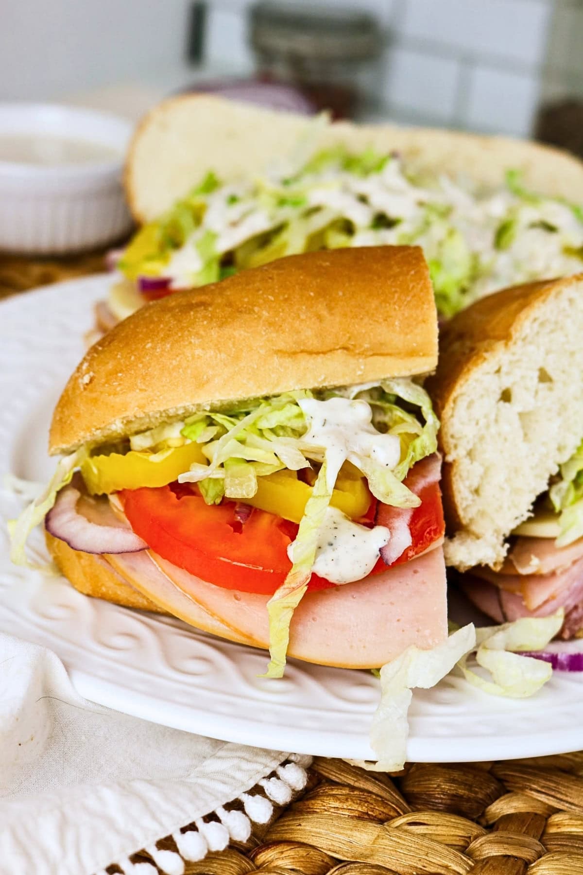 Sub sandwich with ham, tomato, lettuce, and dressing on a white plate.