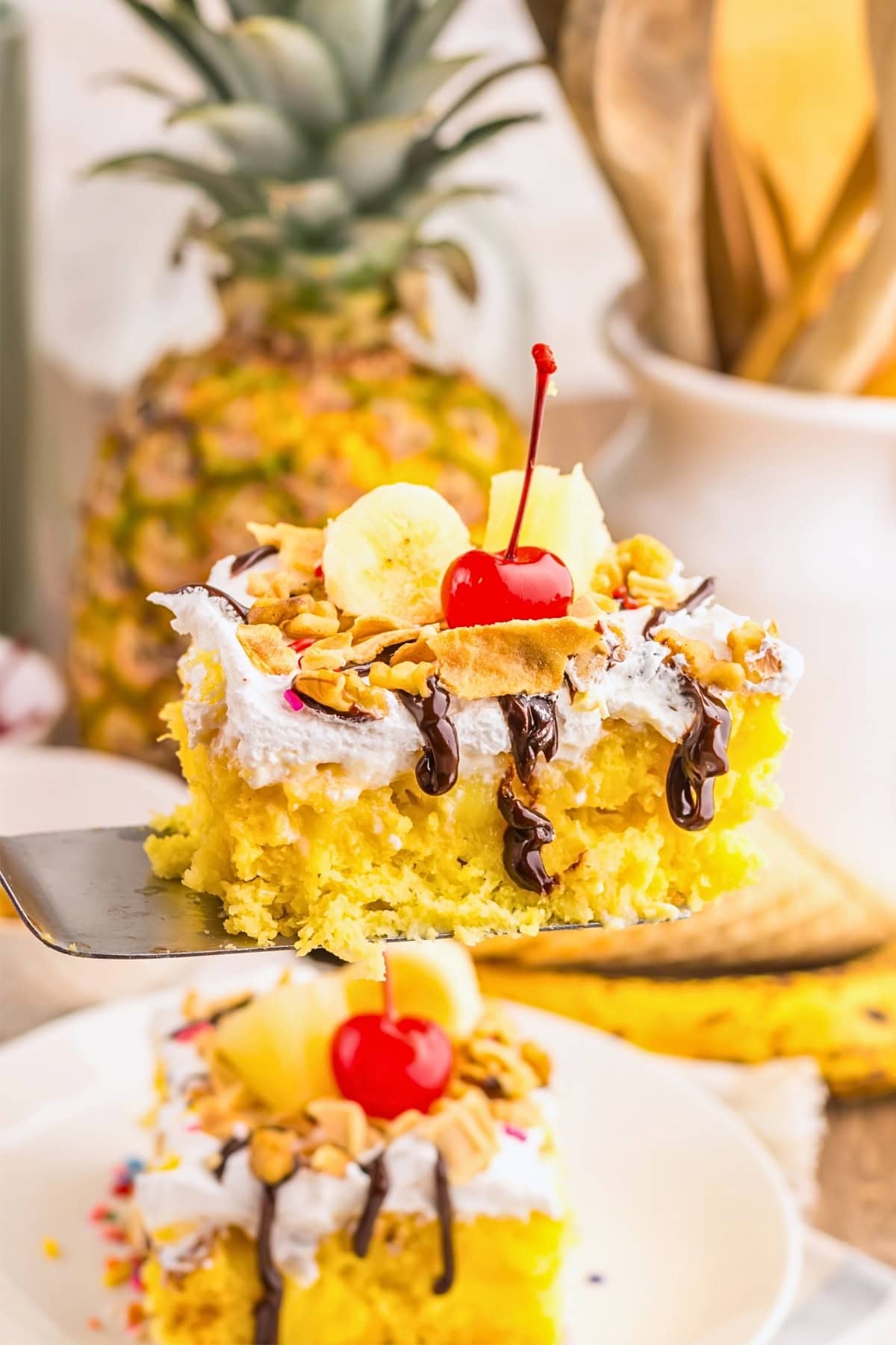 A slice of yellow cake with whipped cream, banana, pineapple, nuts, and a cherry.