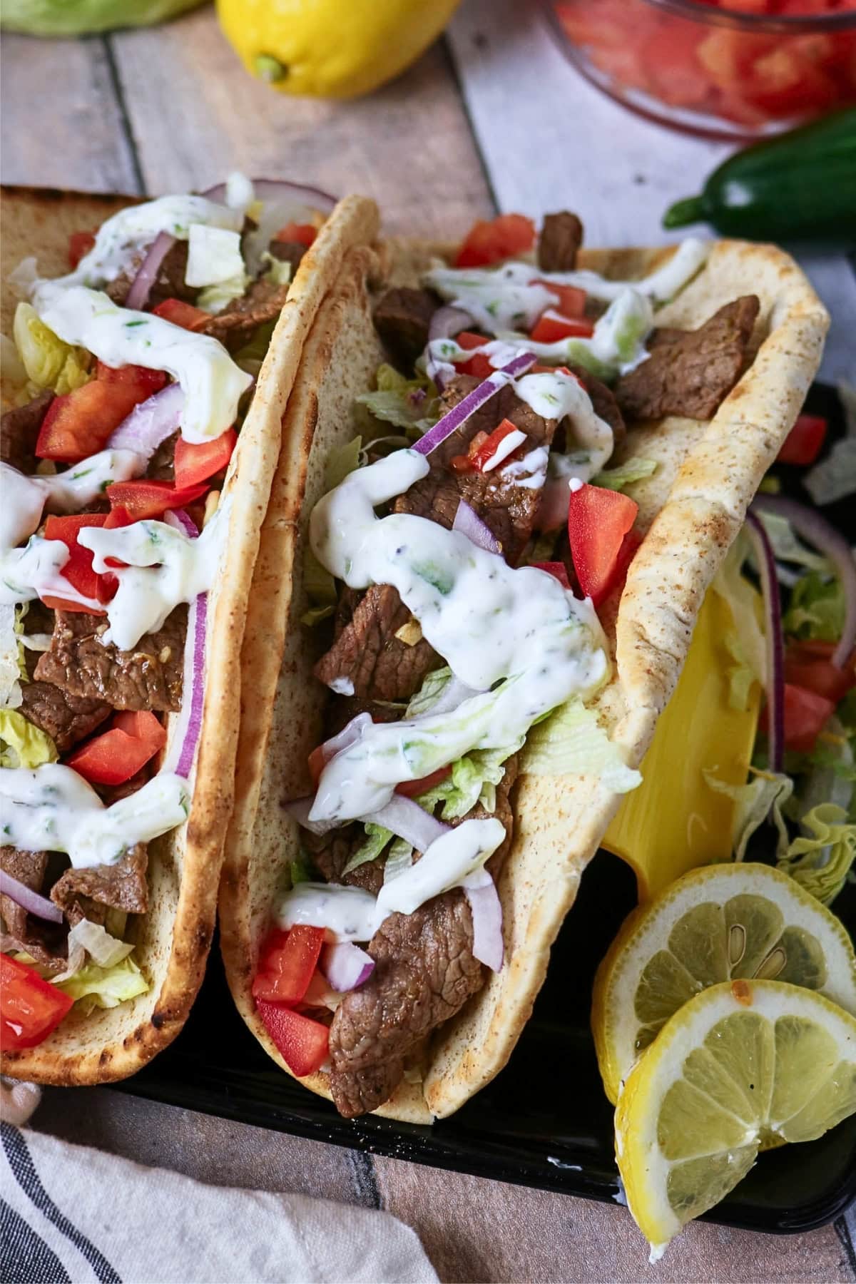Two beef gyros with vegetables and tzatziki sauce, garnished with lemon slices.
