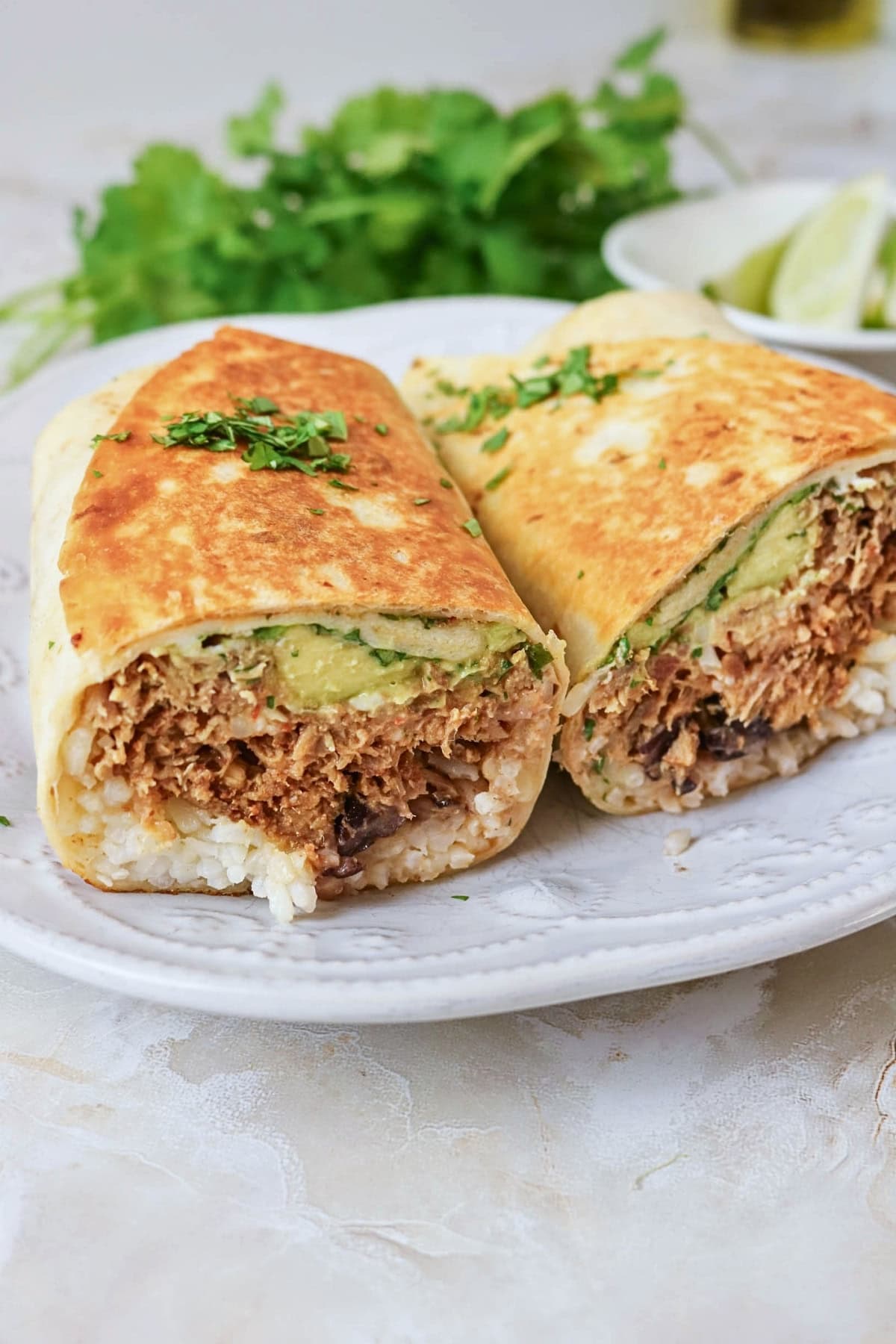A burrito cut in half with rice, shredded meat, and avocado on a white plate.