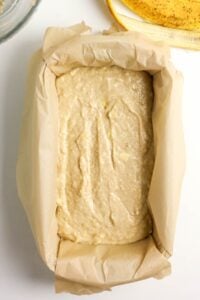 Banana bread batter in a parchment-lined loaf pan, ready to be baked.