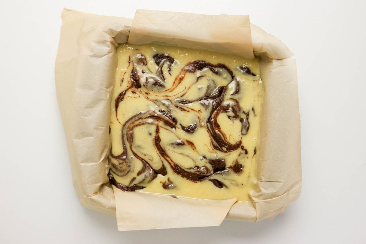 Brownie batter with a swirled design in a parchment-lined square baking pan.