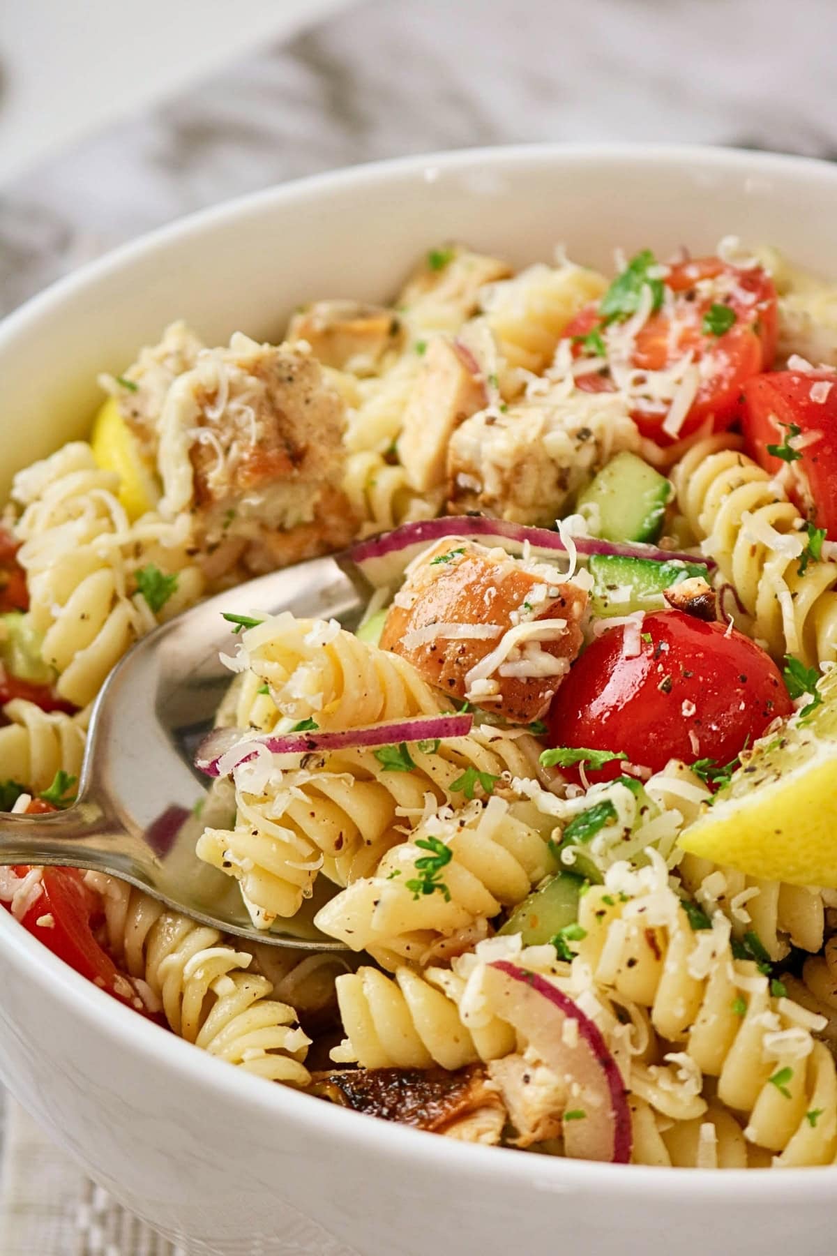 Pasta salad with rotini, chicken, tomatoes, cucumbers, and lemon wedges.