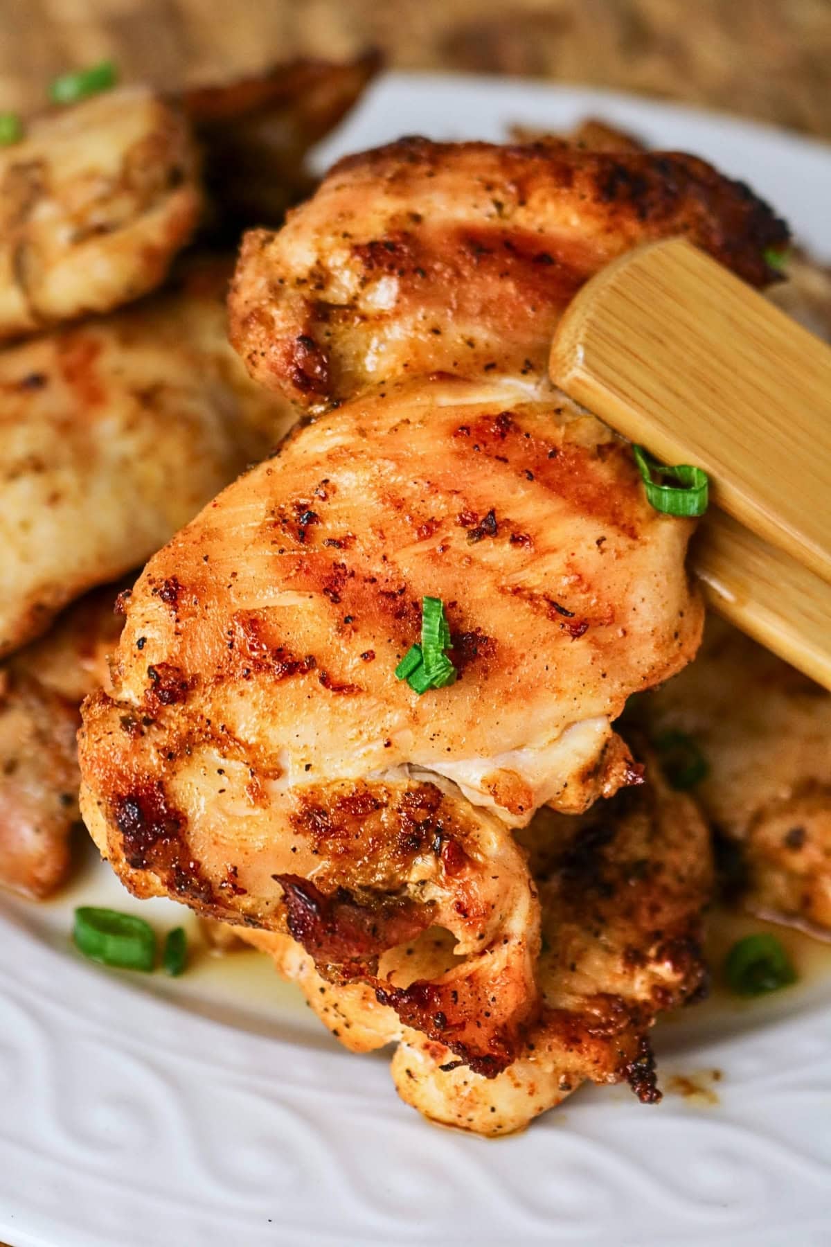 Grilled chicken thighs garnished with chopped green onions on a white plate.