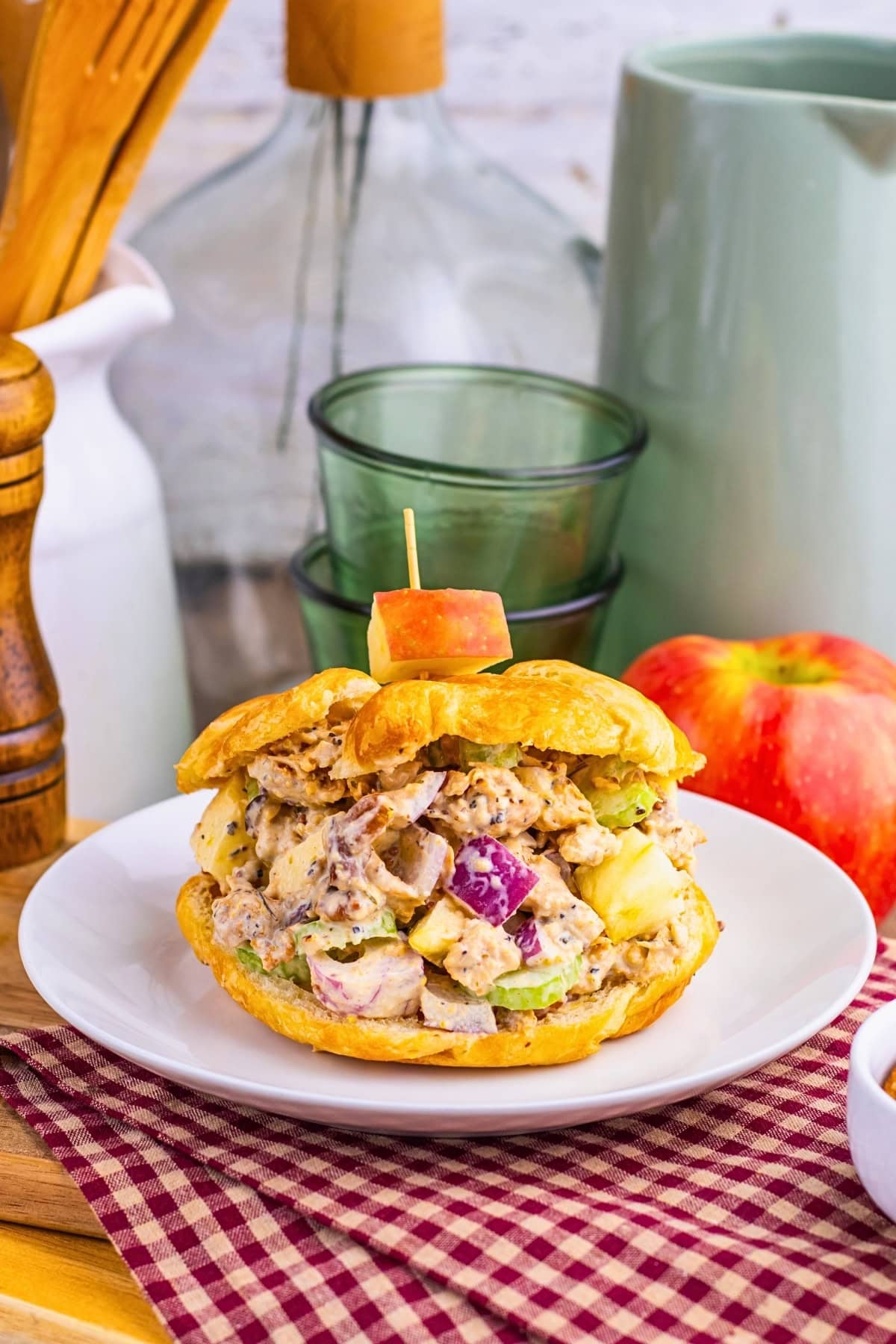 Chicken salad sandwich with apple chunks on a bun, served on a white plate.