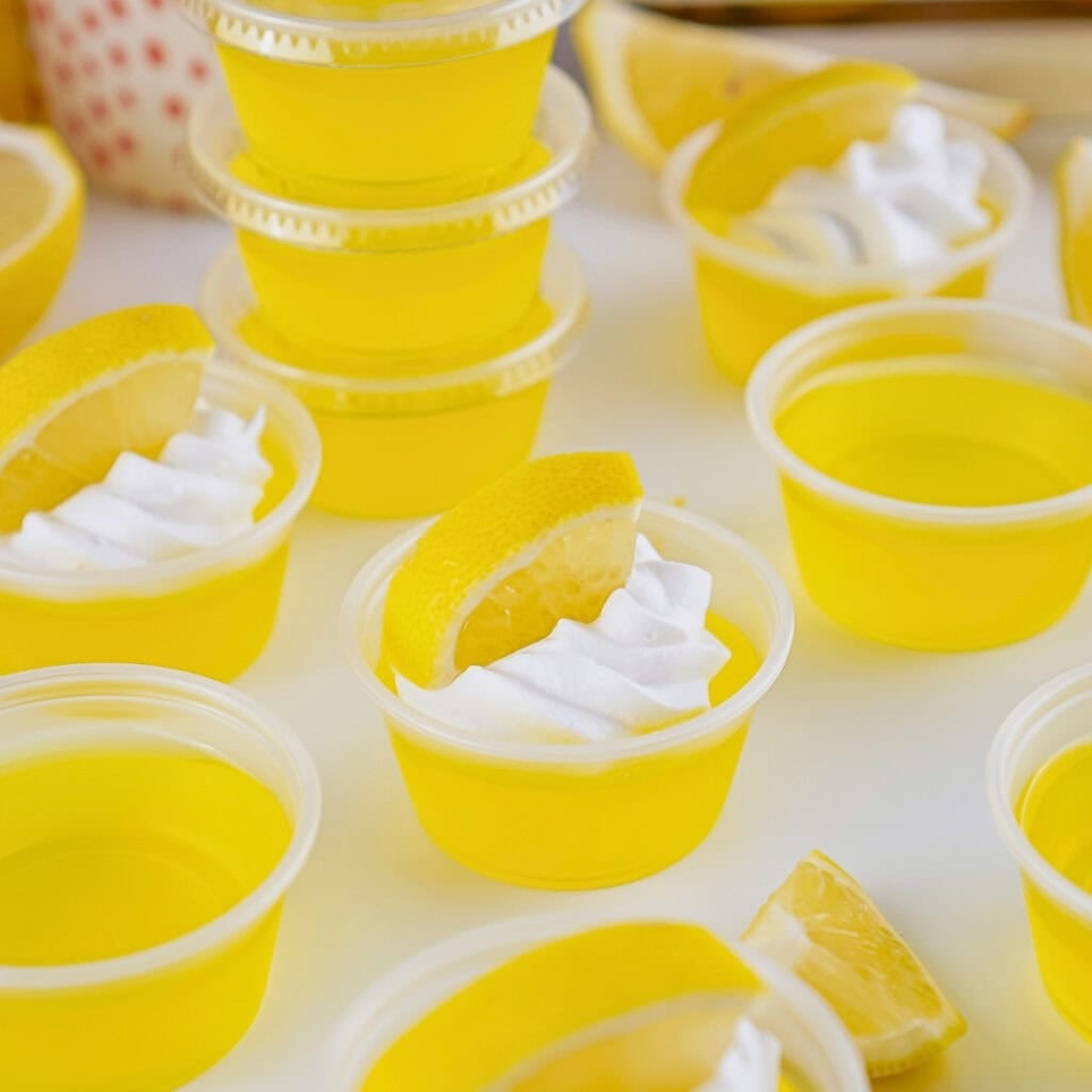 Small cups of yellow gelatin topped with whipped cream and lemon slices.