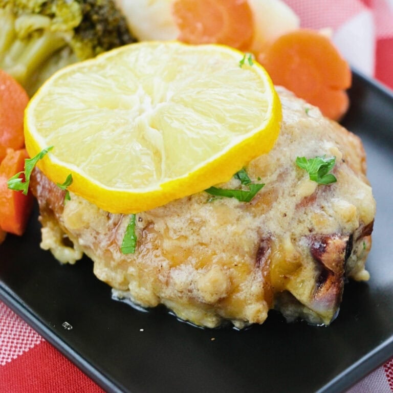 Baked chicken topped with lemon slice, served with carrots and broccoli.