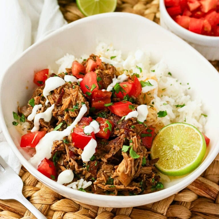 Shredded beef, rice, diced tomatoes, sauce, and lime wedge in a white bowl.