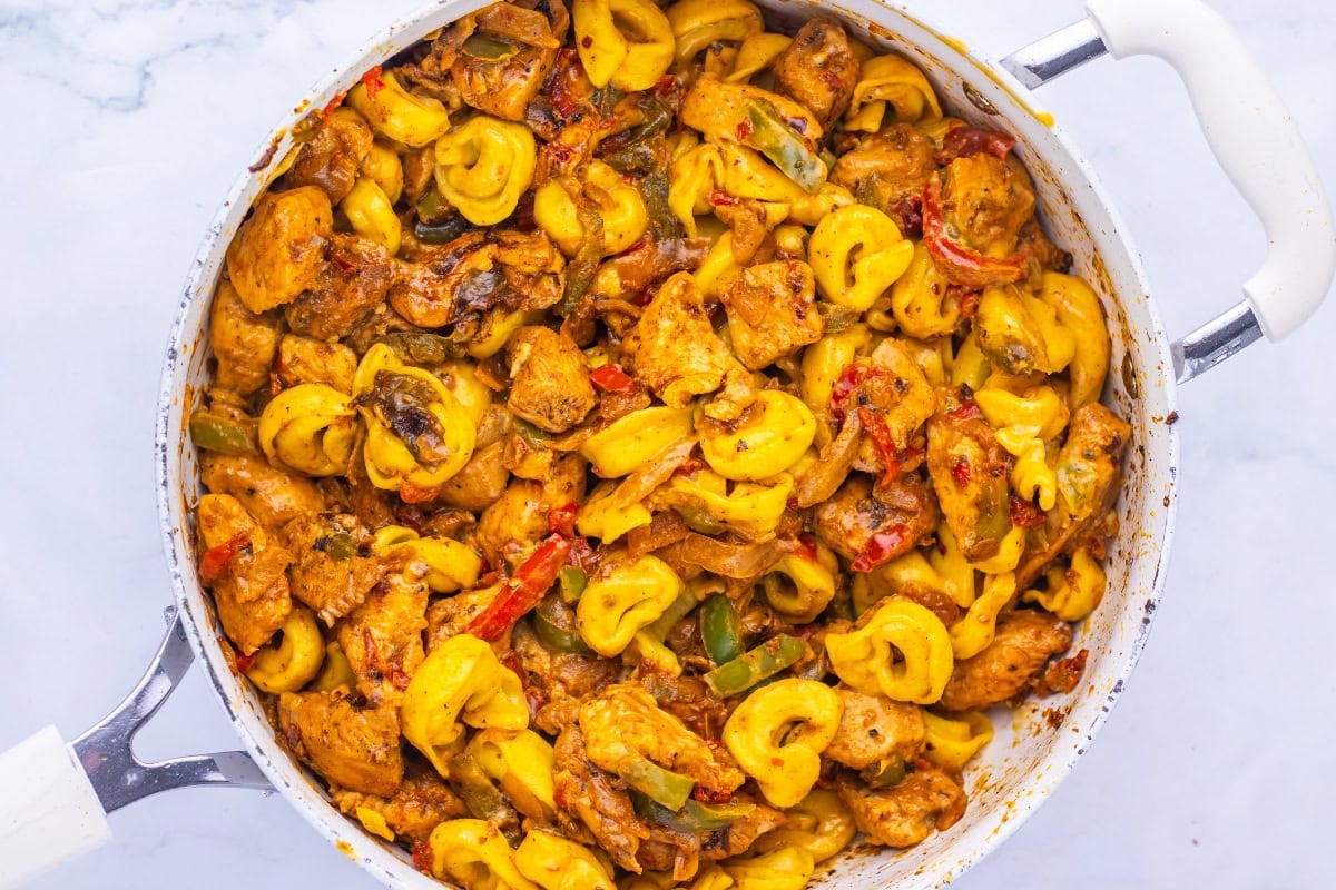 A pan of creamy tortellini pasta with chicken, mushrooms, and peppers.
