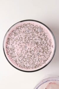 A glass of pink smoothie topped with chia seeds, viewed from above.