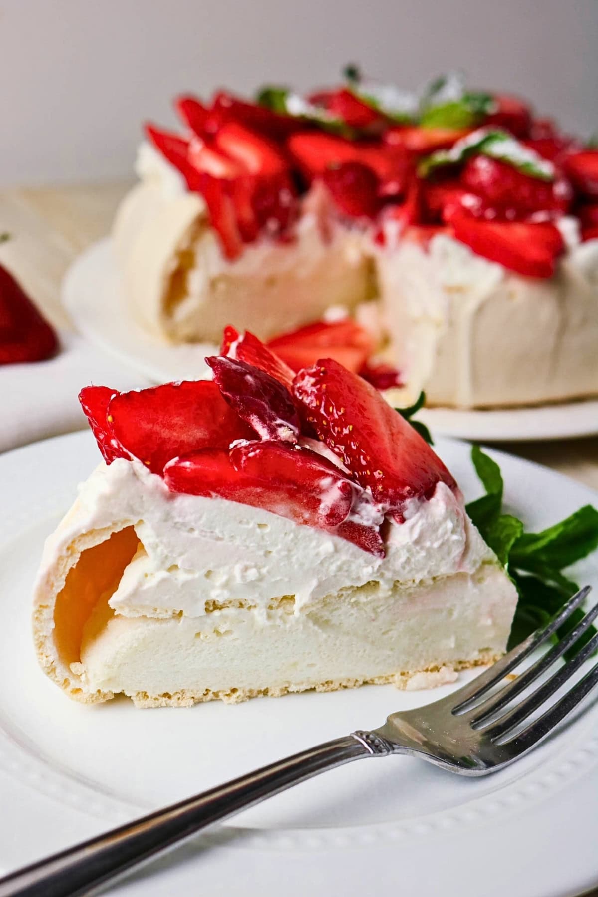 Slice of pavlova topped with whipped cream and fresh strawberries on a plate.