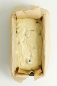 Loaf pan lined with parchment paper filled with raw batter containing berries.