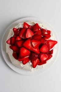 A pavlova dessert topped with whipped cream and fresh sliced strawberries.