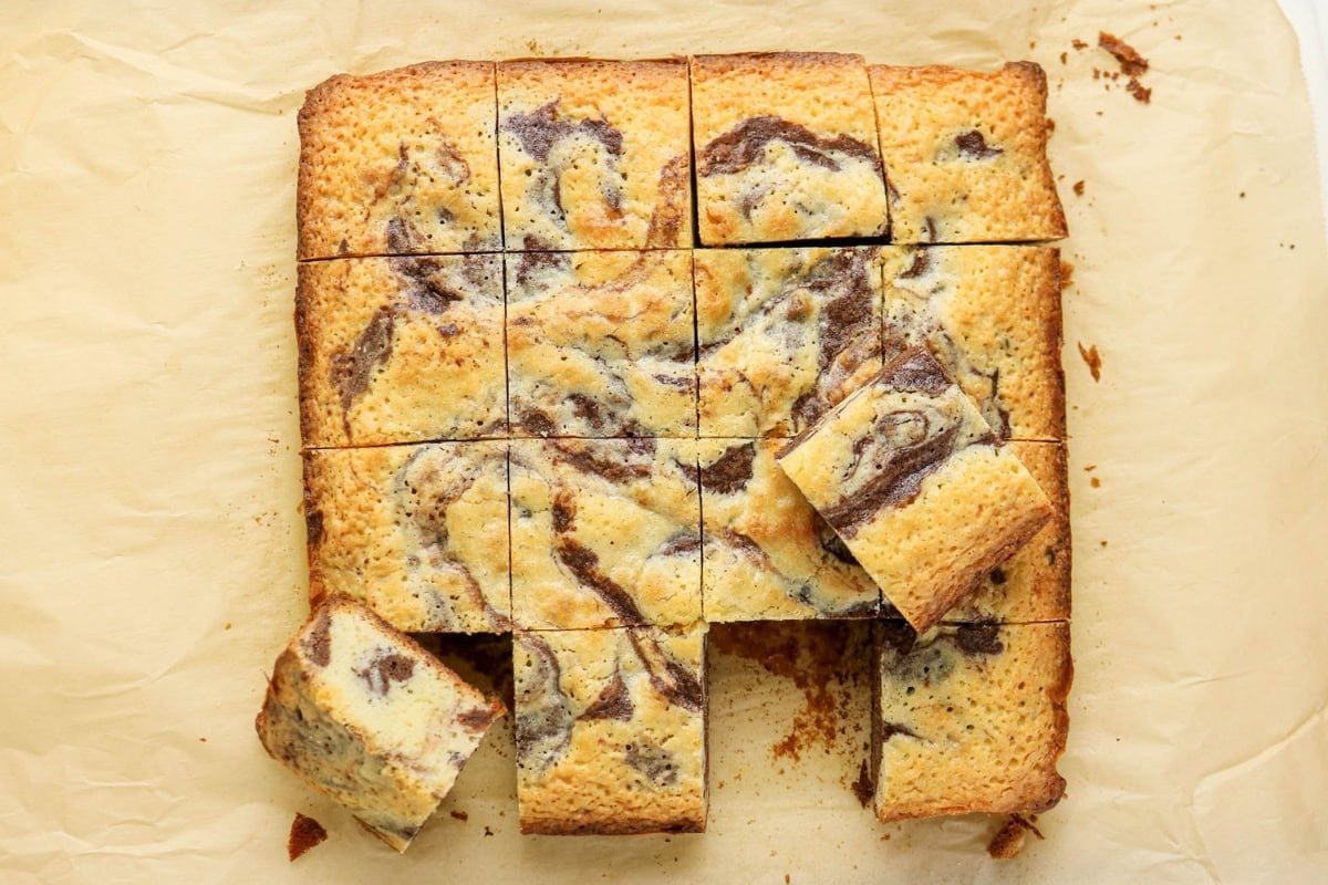 Marble swirled cake cut into square pieces on parchment paper.