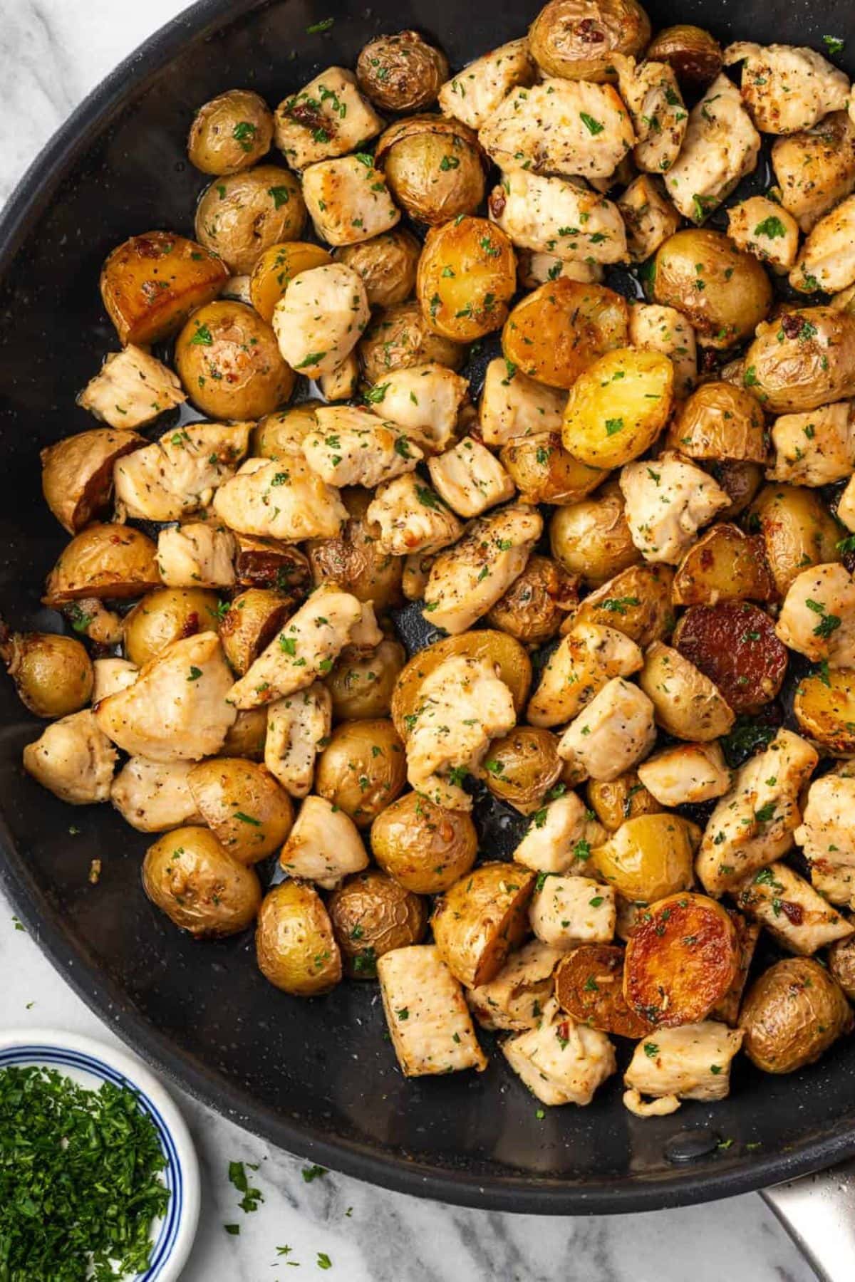 Cooked chicken and roasted baby potatoes mixed with herbs in a skillet.