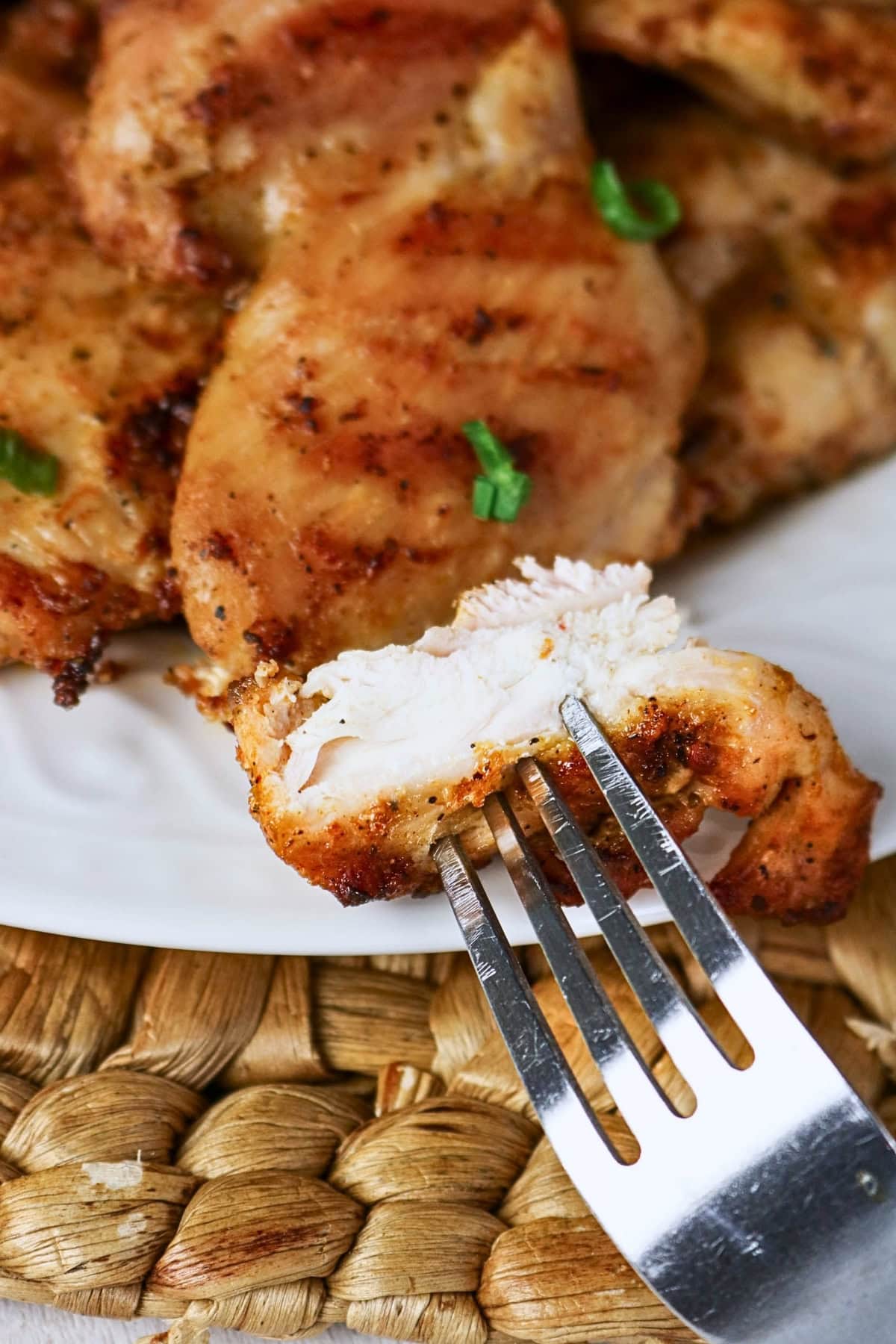 A fork holds a juicy, cooked piece of seasoned chicken breast on a plate.