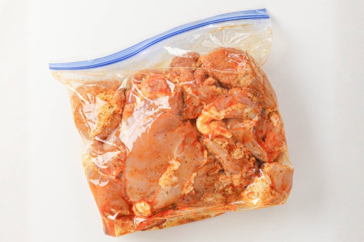 Raw marinated chicken pieces in a sealed plastic zip-top bag.