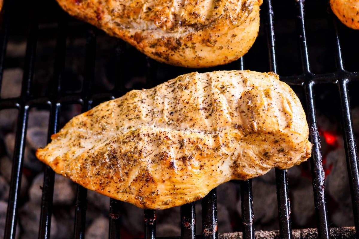 Grilled, seasoned chicken breast cooking on a barbecue grill.