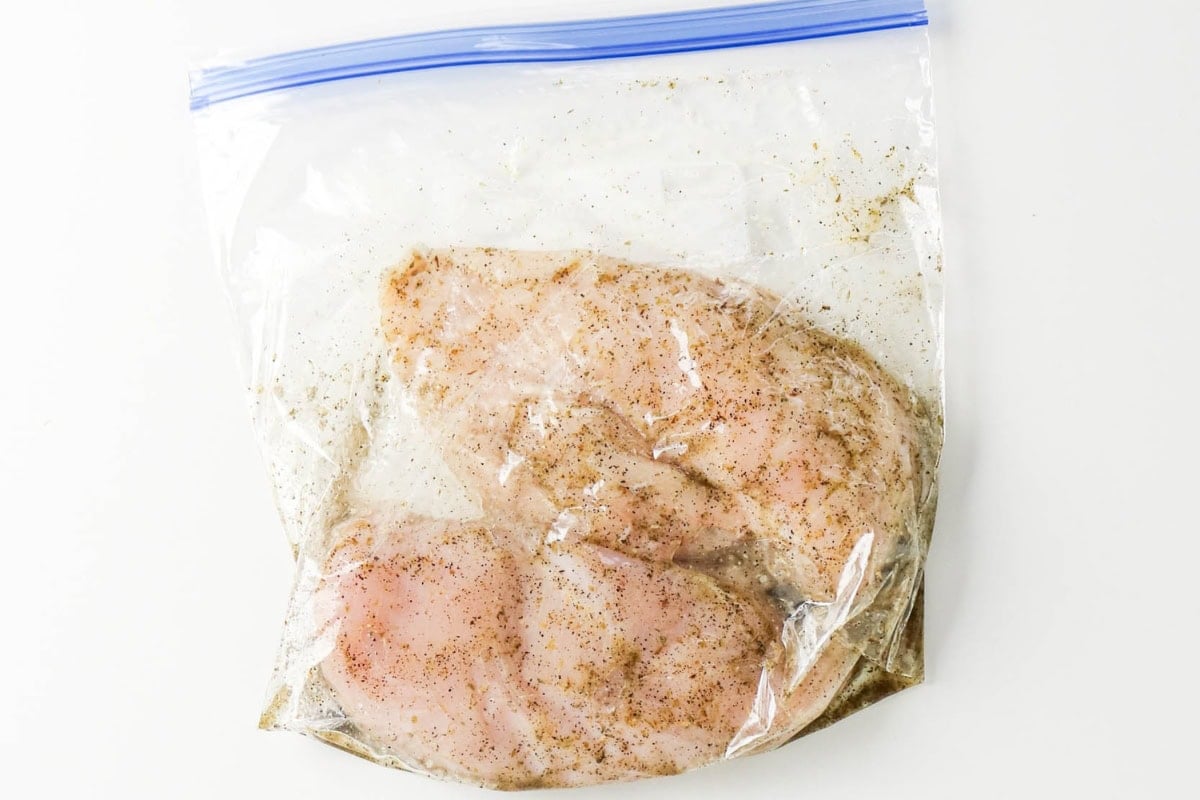 Raw chicken breasts marinating in a sealed plastic zip-top bag.