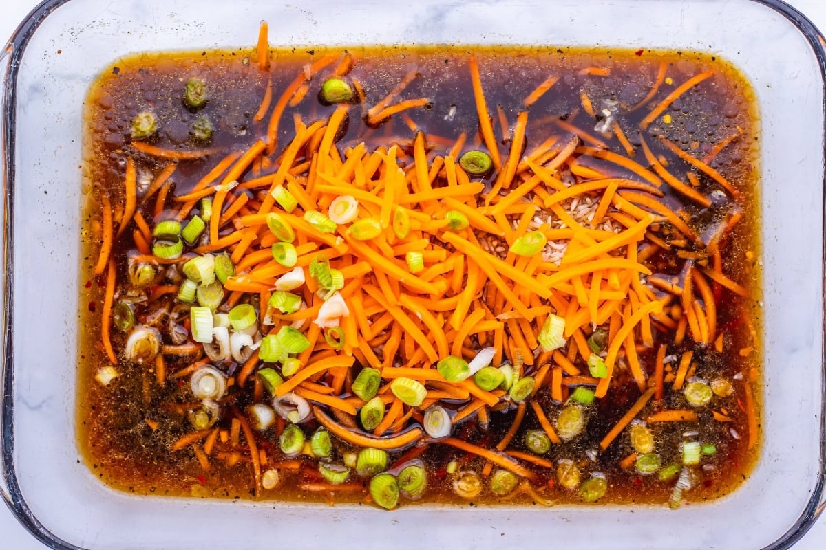 Shredded carrots and chopped green onions in a dark marinade in a glass dish.
