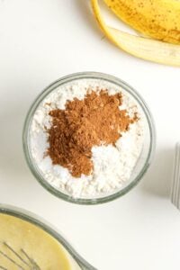 A bowl of flour and cinnamon on a white surface, with a banana peel nearby.
