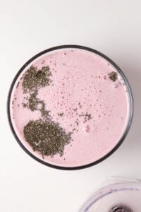 A glass of pink smoothie topped with chia seeds, viewed from above.