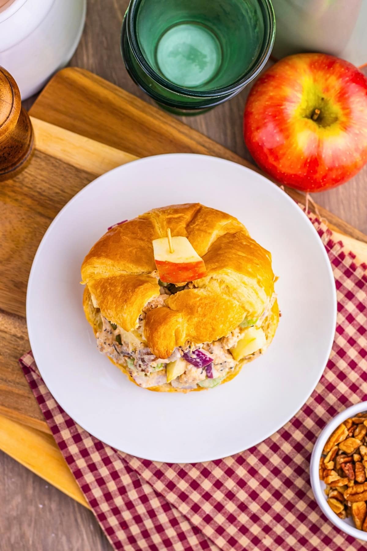 A croissant sandwich on a white plate, with an apple slice on top, overhead view.