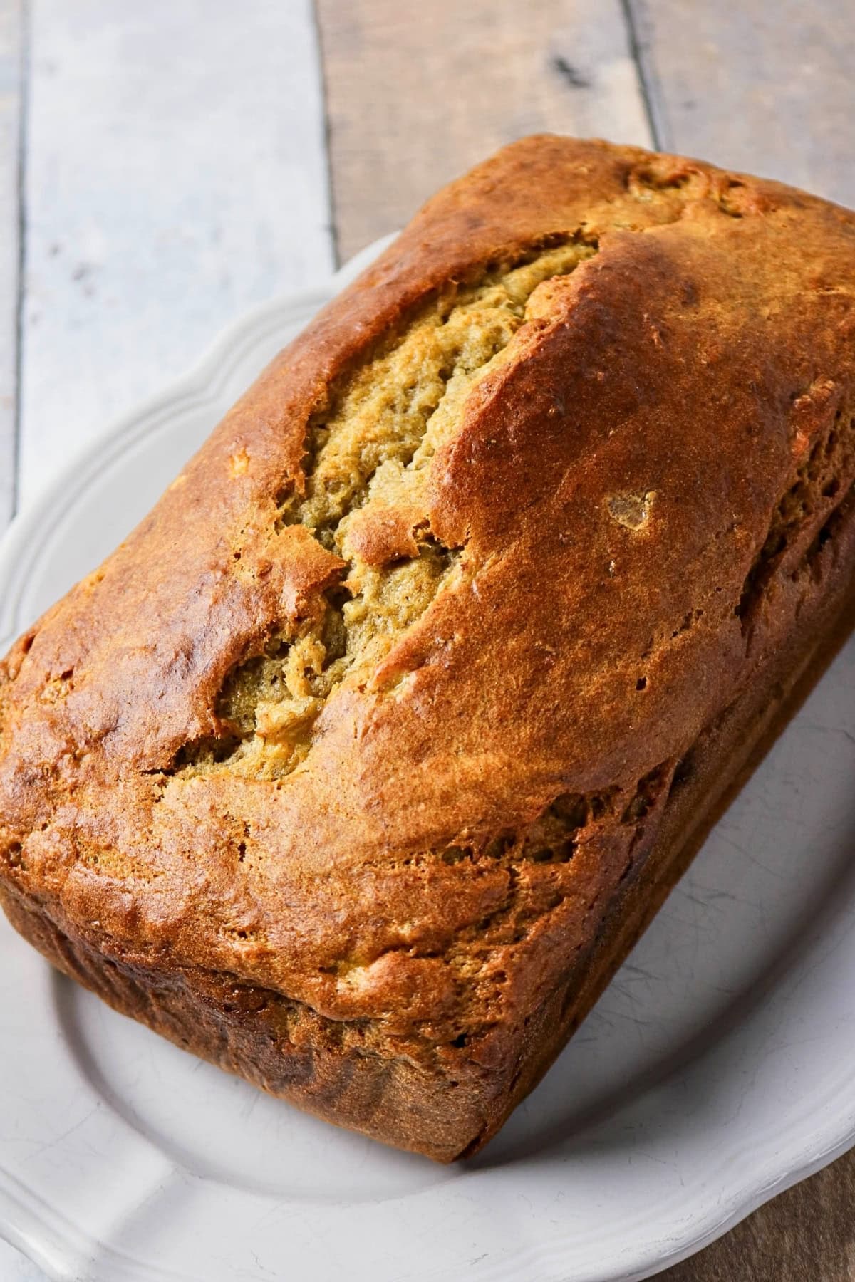 A loaf of golden-brown banana bread on a white plate.