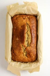 Golden brown loaf of bread in a parchment-lined baking tin, viewed from above.