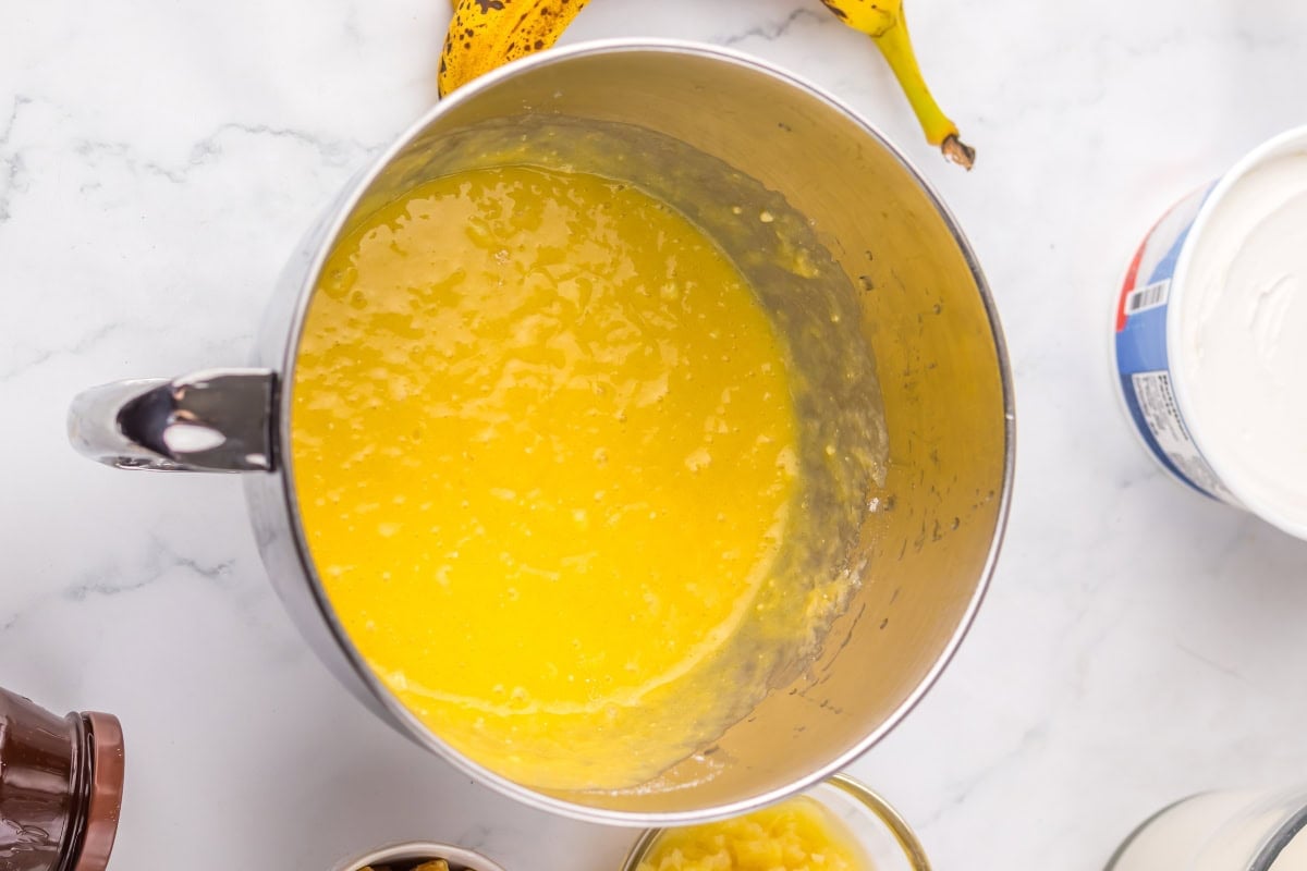 Mixing bowl filled with yellow banana pudding mixture on a marble counter.