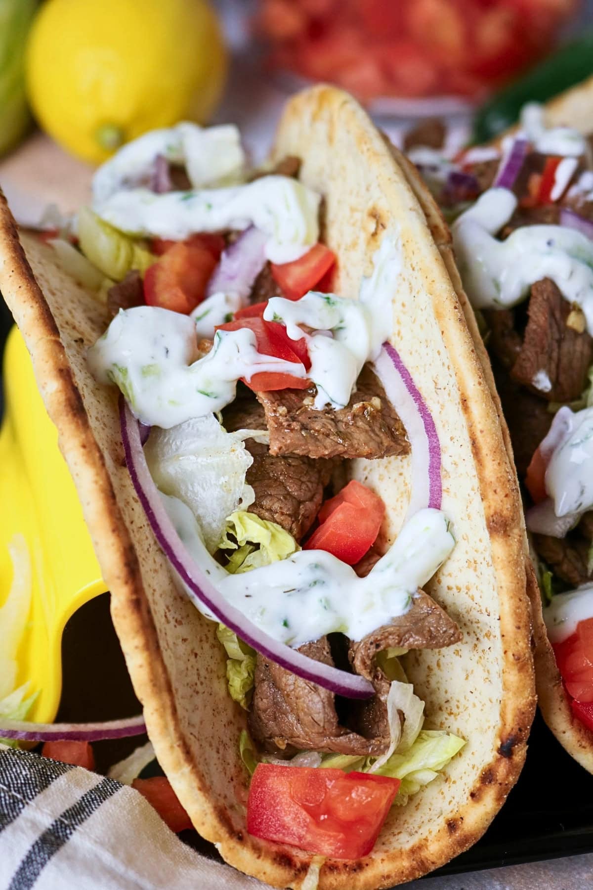 A pita wrap with beef, lettuce, tomato, red onion, and creamy white sauce.