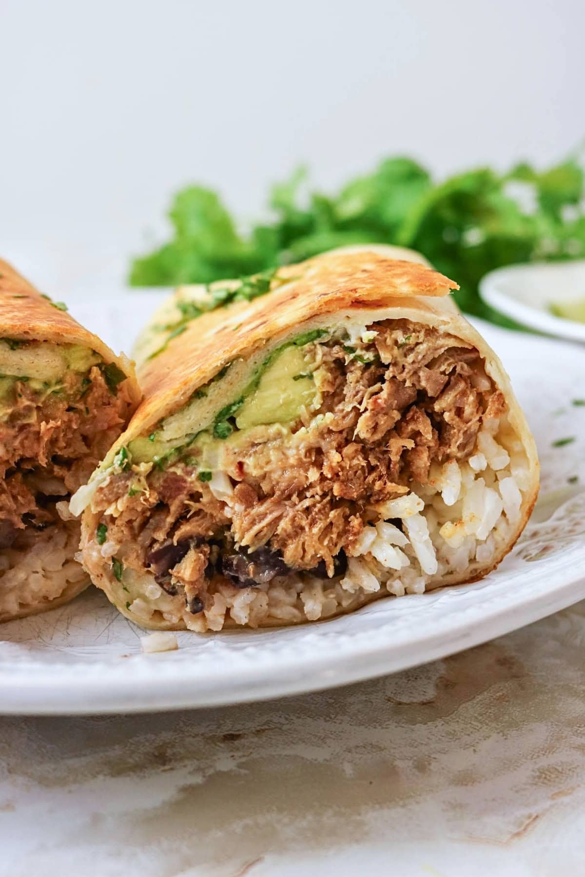 A burrito cut in half showing rice, shredded meat, and avocado inside.