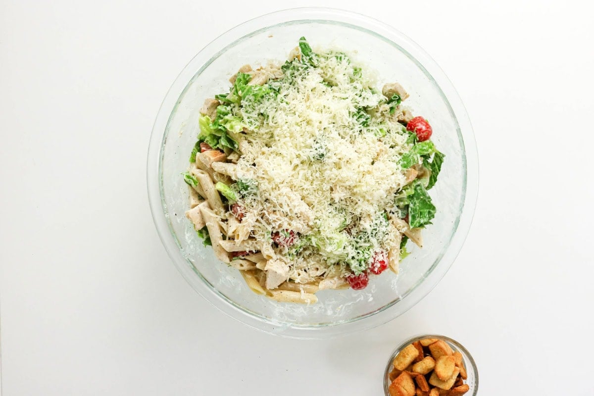 A bowl of Caesar salad with grated cheese and a small bowl of croutons.