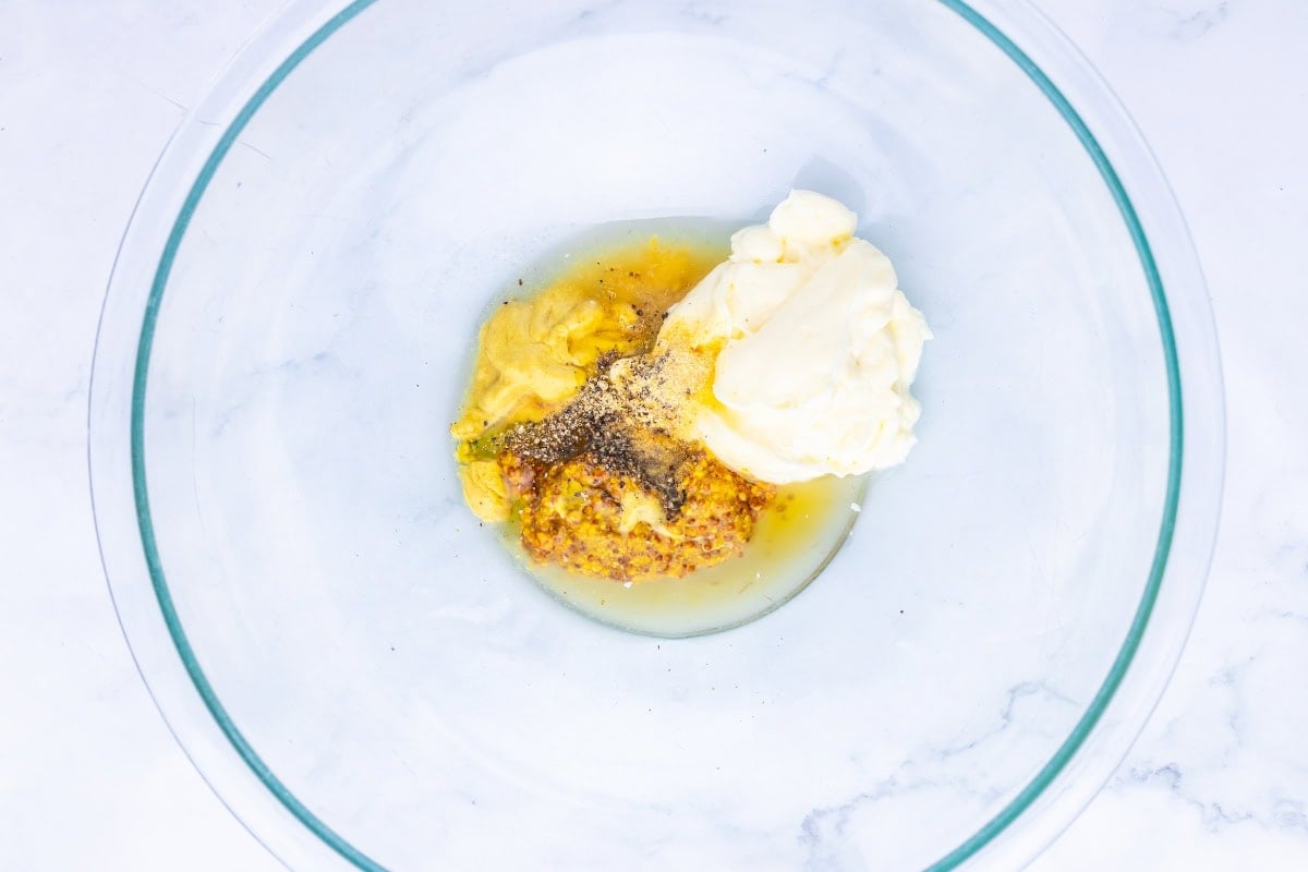 A glass bowl with mustard, mayonnaise, and pepper on a white surface.