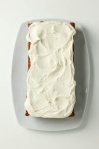 Rectangular loaf cake with white frosting on a white plate, viewed from above.
