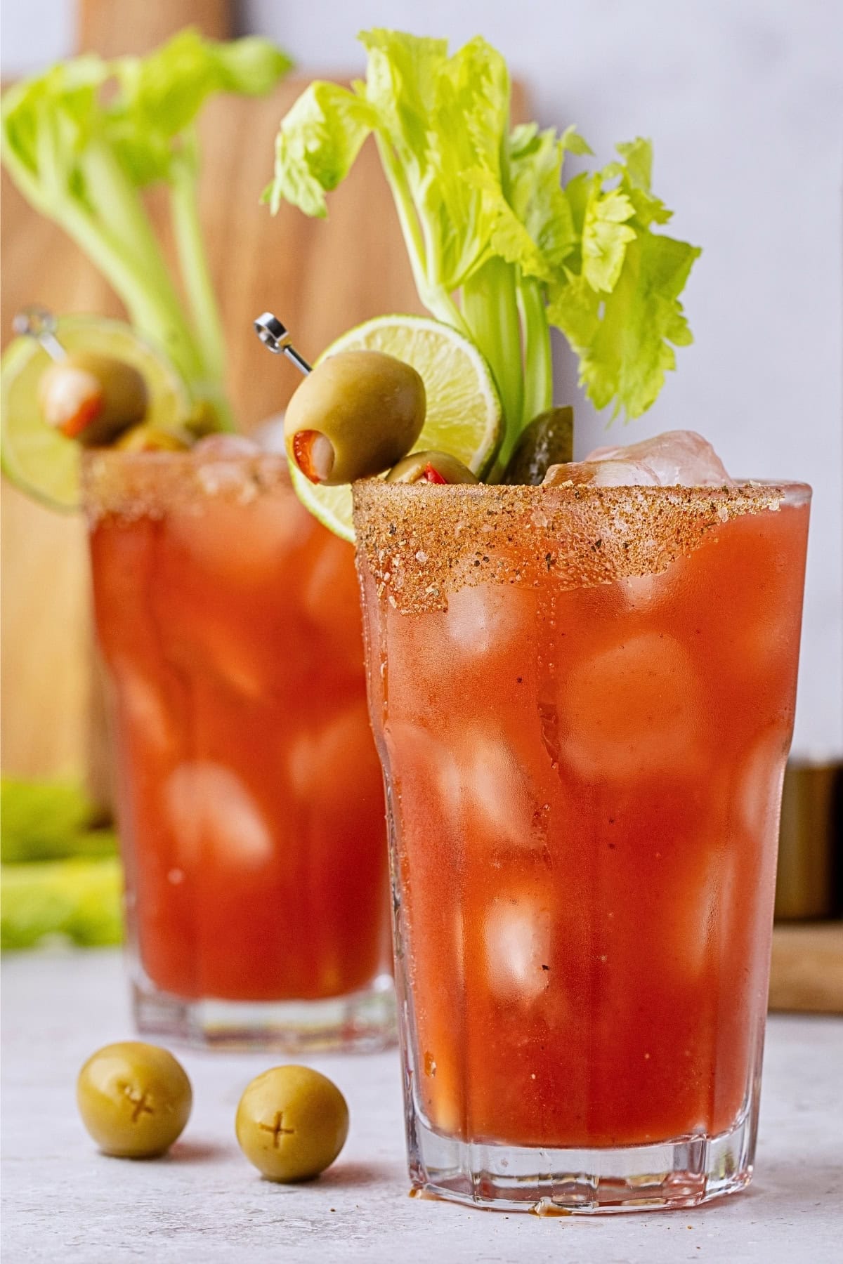 Two Bloody Mary cocktails garnished with celery, olives, and lime slices.