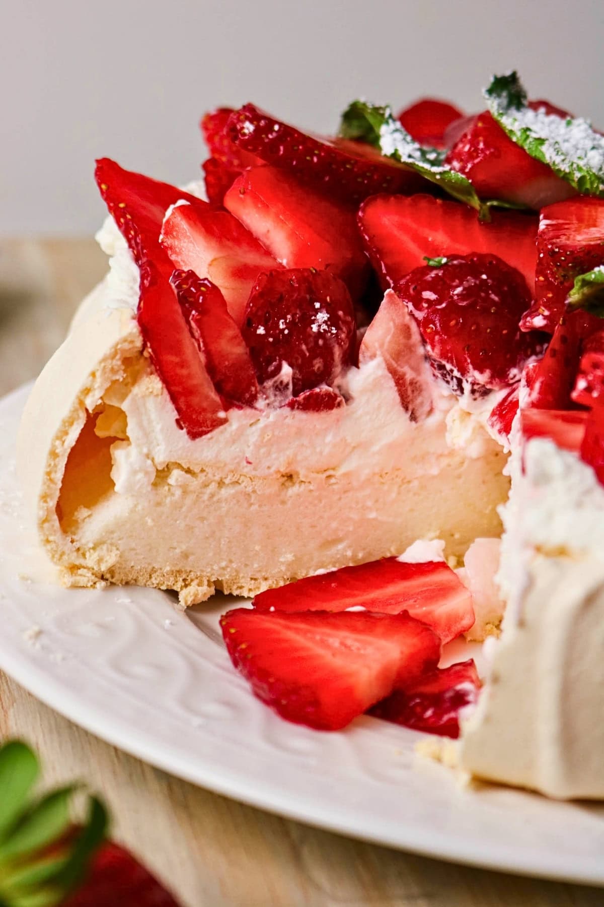 A pavlova topped with whipped cream and fresh sliced strawberries on a plate.