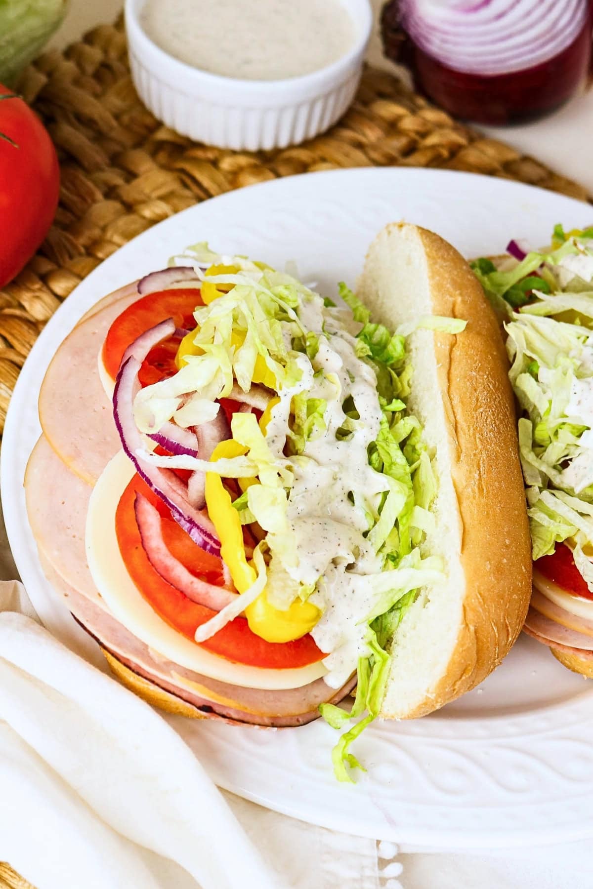 A sub sandwich with lettuce, tomato, onions, and creamy dressing on a plate.