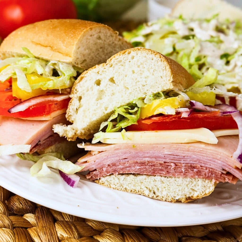 A deli sandwich with ham, cheese, lettuce, tomato, and onions on a plate.