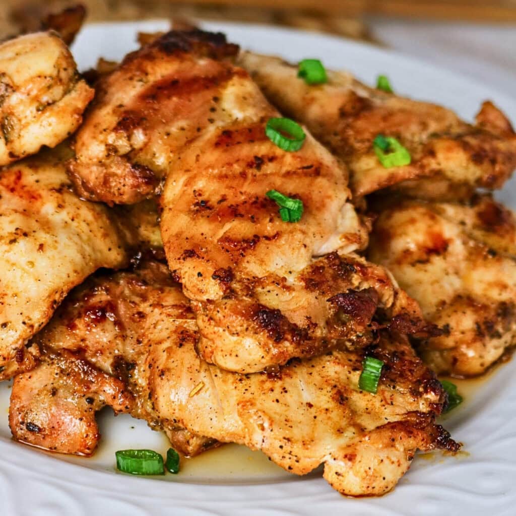 Grilled chicken thighs garnished with chopped green onions on a white plate.